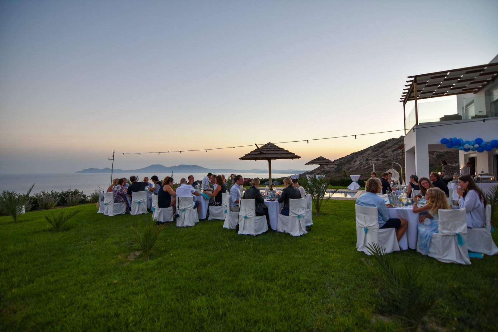 Guests dining on the lawn at sunset with sea view